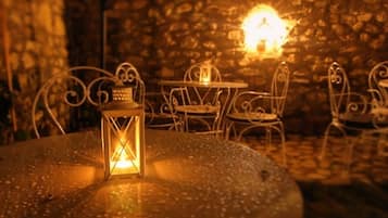 Una mesa redonda con un farol en primer plano, rodeada de sillas de metal.