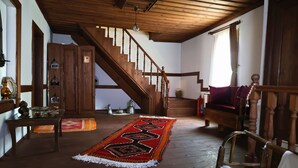 A spacious living room with a wooden staircase, a red patterned rug, and a wooden chair. - Ahşena Bağ Badeli Konak Safranbolu (Safranbolu)