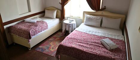 A hotel room with two single beds, a small round table, and a window with curtains.
