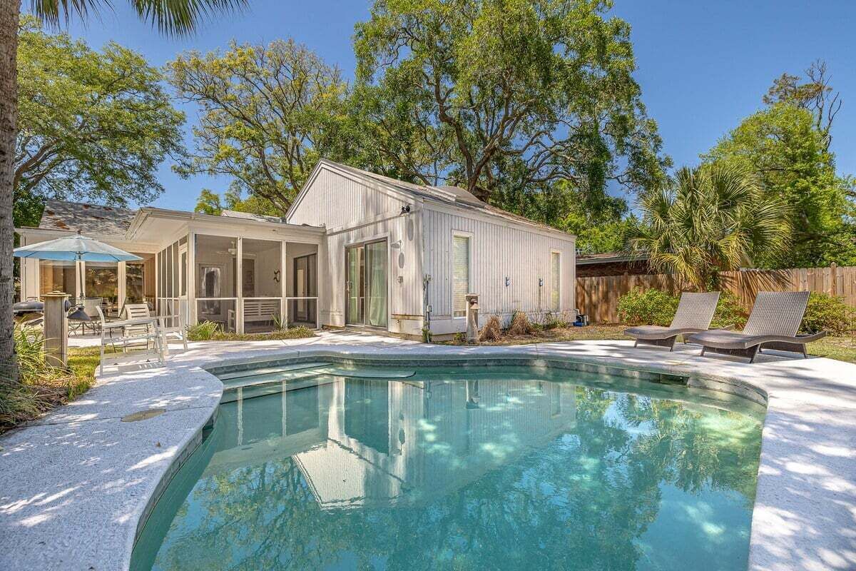 A swimming pool with a house in the background, surrounded by trees and a wooden fence.