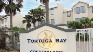 A sign for TORTUGA BAY condominiums with a turtle logo. - Bay Front: Gradual-Entry Pool: Boat Slip (South Padre Island)