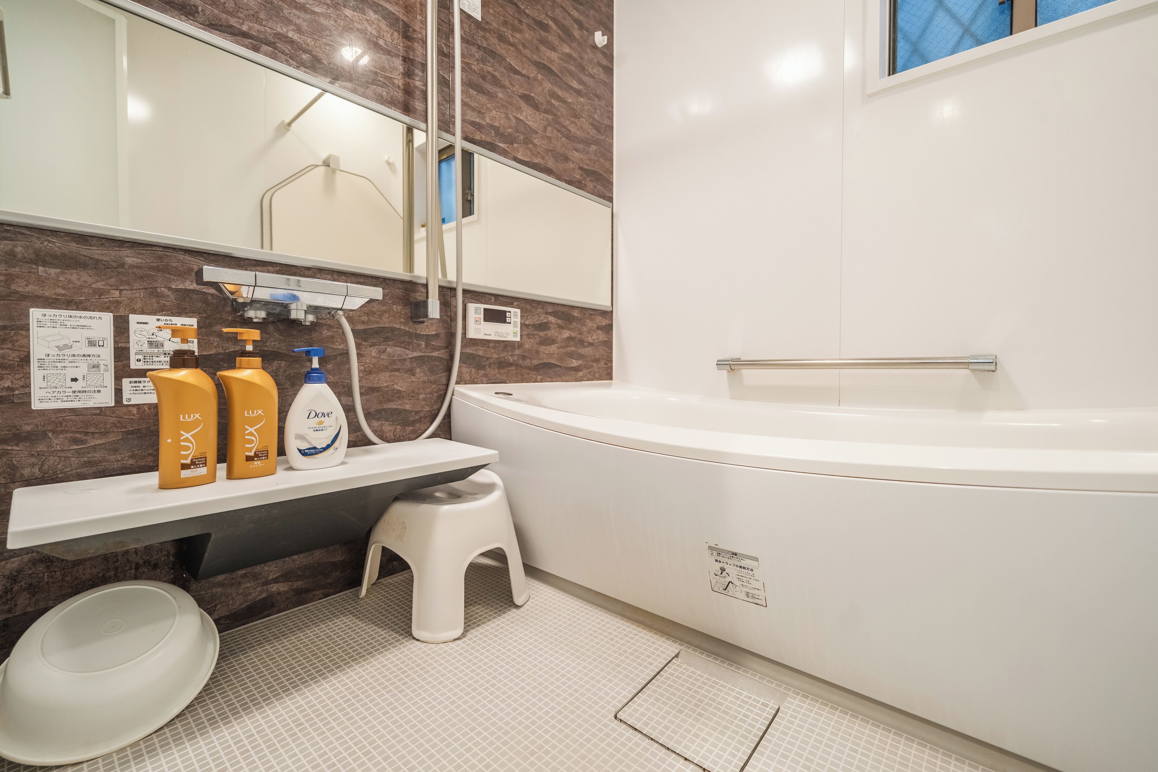 Ein modernes Badezimmer mit einer weißen Badewanne, einem Waschtisch mit Pflegeprodukten, einem kleinen Hocker und einem Spiegel.