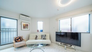 Ein modernes Wohnzimmer mit einer Couch, einem Glastisch, einem Fernseher und einem großen Fenster.