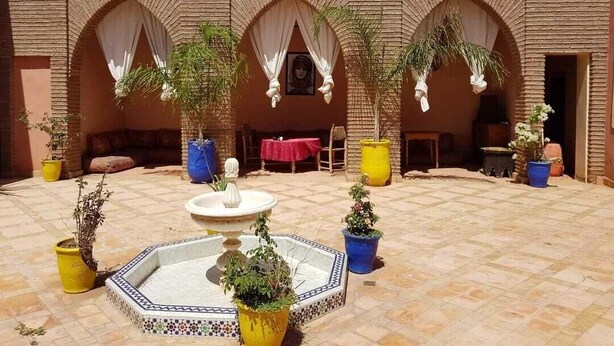 A courtyard with a fountain, potted plants, and a brick wall with arches. - Riad Sidi Hicham (Villa avec piscine sans vis à vis ) (MARRAKECH)