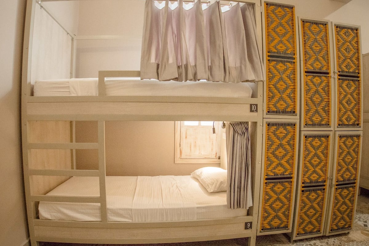 A bunk bed room with a window, curtains, and a patterned door.