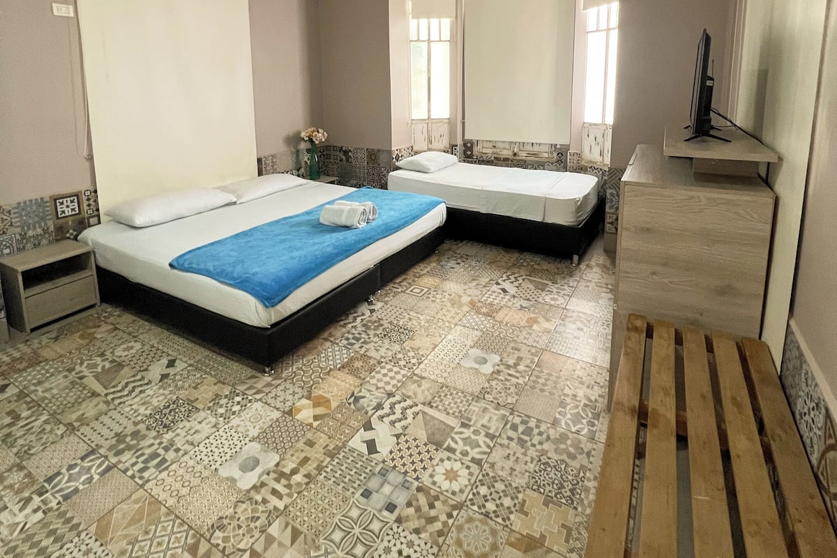 A bedroom with two beds, a ceiling fan, a mirror, a TV, and patterned floor tiles.