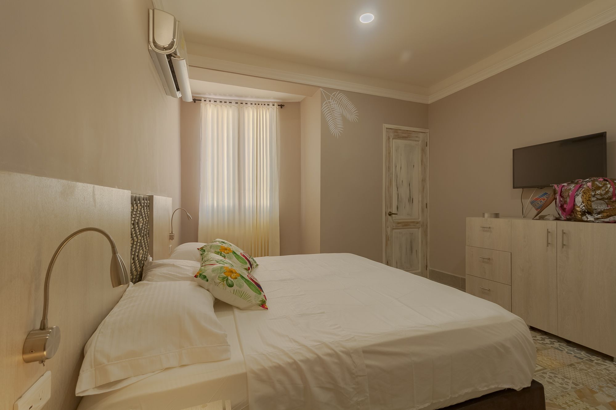 A bedroom with a bed, a bedside table, a wardrobe, a television, and a window with curtains.