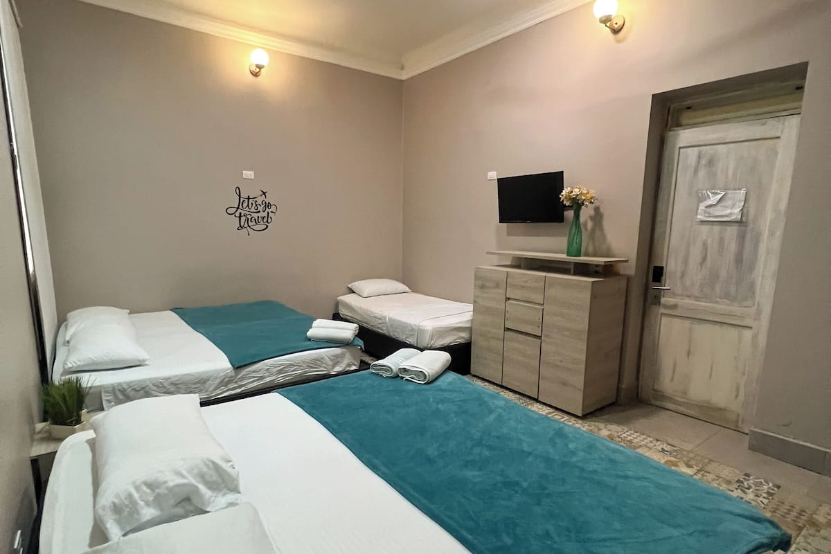 A hotel room with two beds, a ceiling fan, a flat-screen TV, a small cabinet, and a door.
