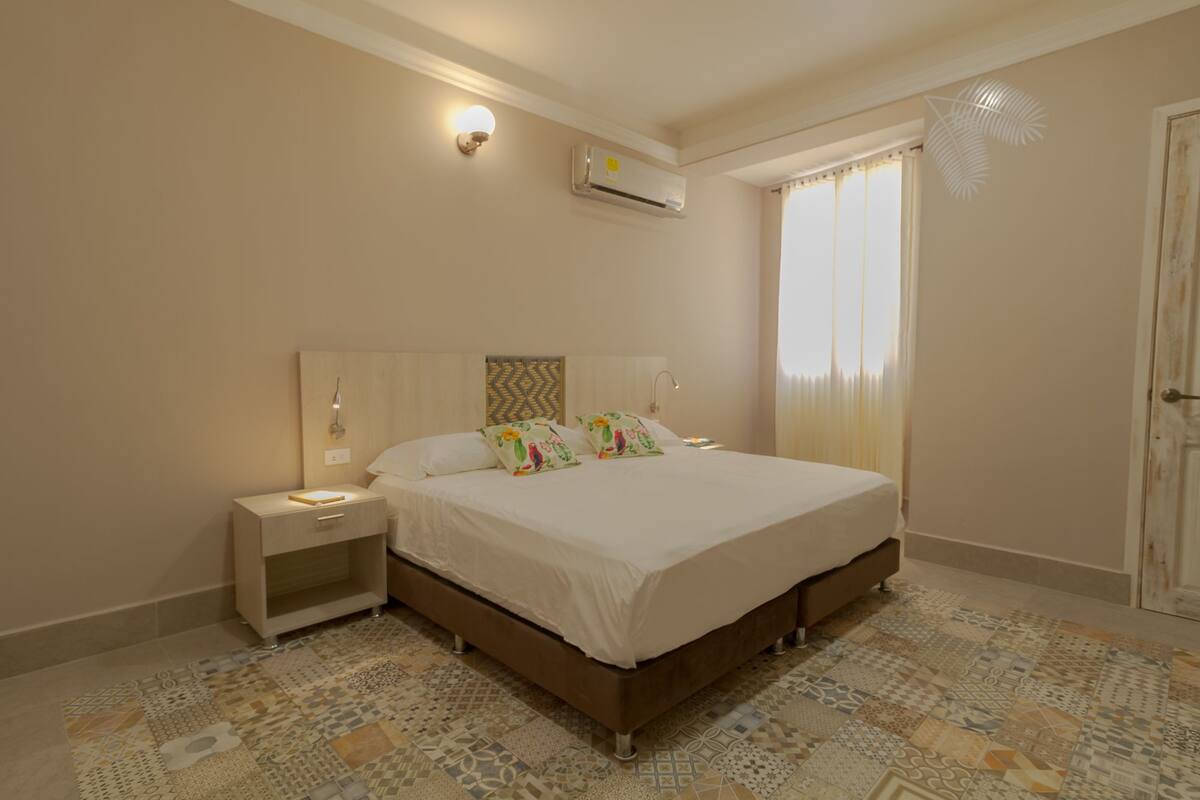 A bedroom with a bed, nightstand, wall-mounted air conditioner, and patterned floor tiles.