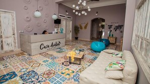 Un hall d’hôtel comprenant un comptoir d’accueil, un sol aux motifs colorés, un canapé avec des coussins et un ventilateur de plafond.