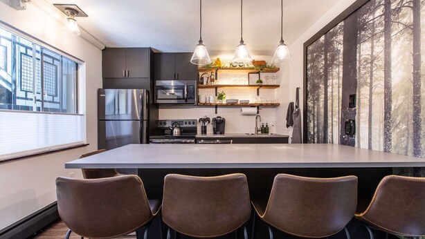 Una cocina moderna con una isla grande, taburetes de bar, electrodomésticos de acero inoxidable e iluminación colgante.