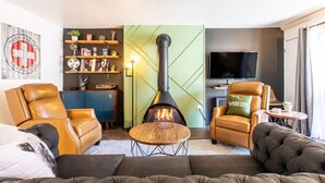 Una sala de estar moderna con sofás de cuero, un hogar central de leña, un televisor y una estantería.