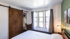 Un dormitorio con una cama grande, un armario de madera, una silla y un ventanal con cortinas.