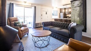 Una sala moderna con un sofá, sillones y una mesa de centro. Cuenta con una zona de cocina con un refrigerador y microondas.