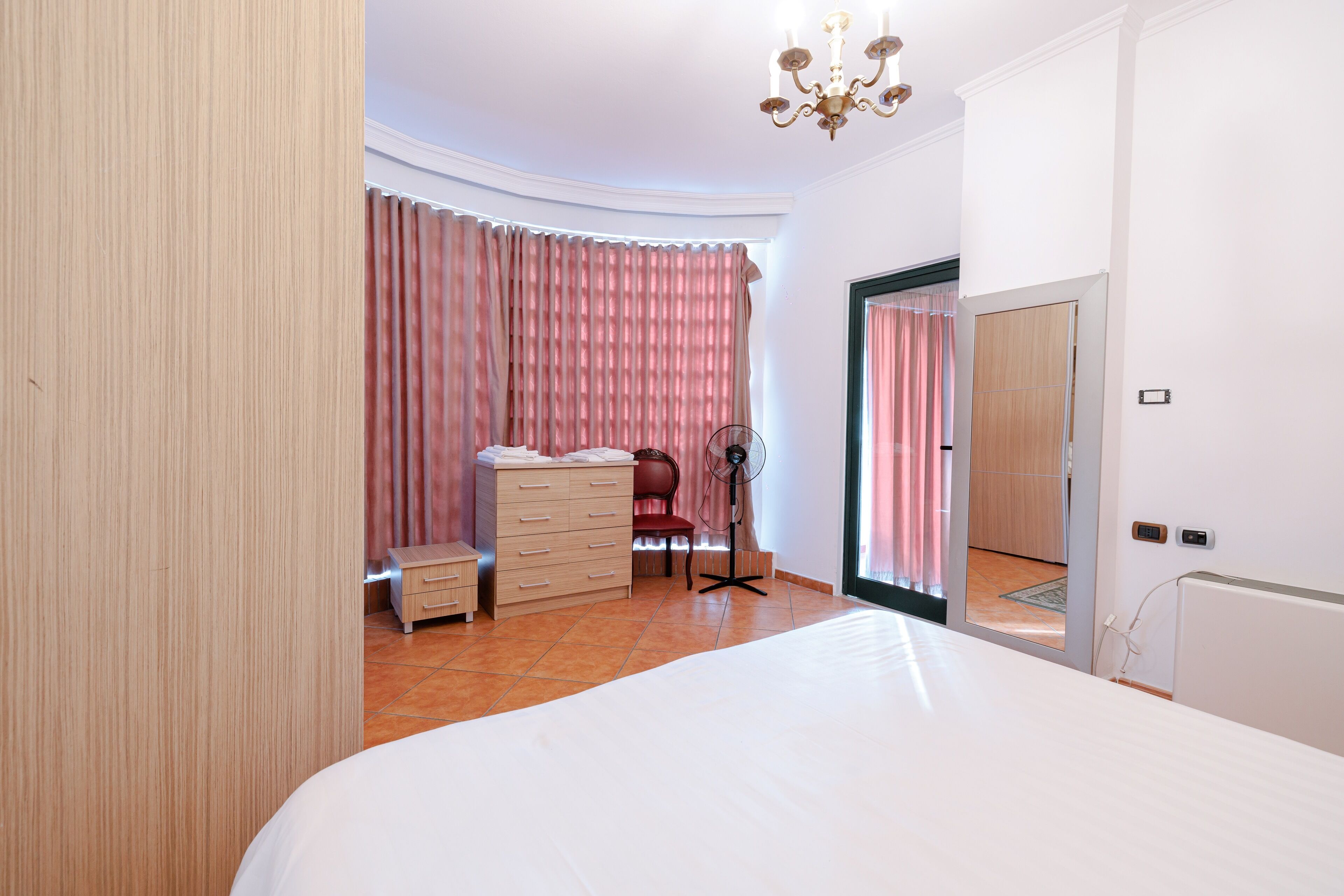 Une chambre à coucher avec un grand lit, une commode, une chaise et un ventilateur.