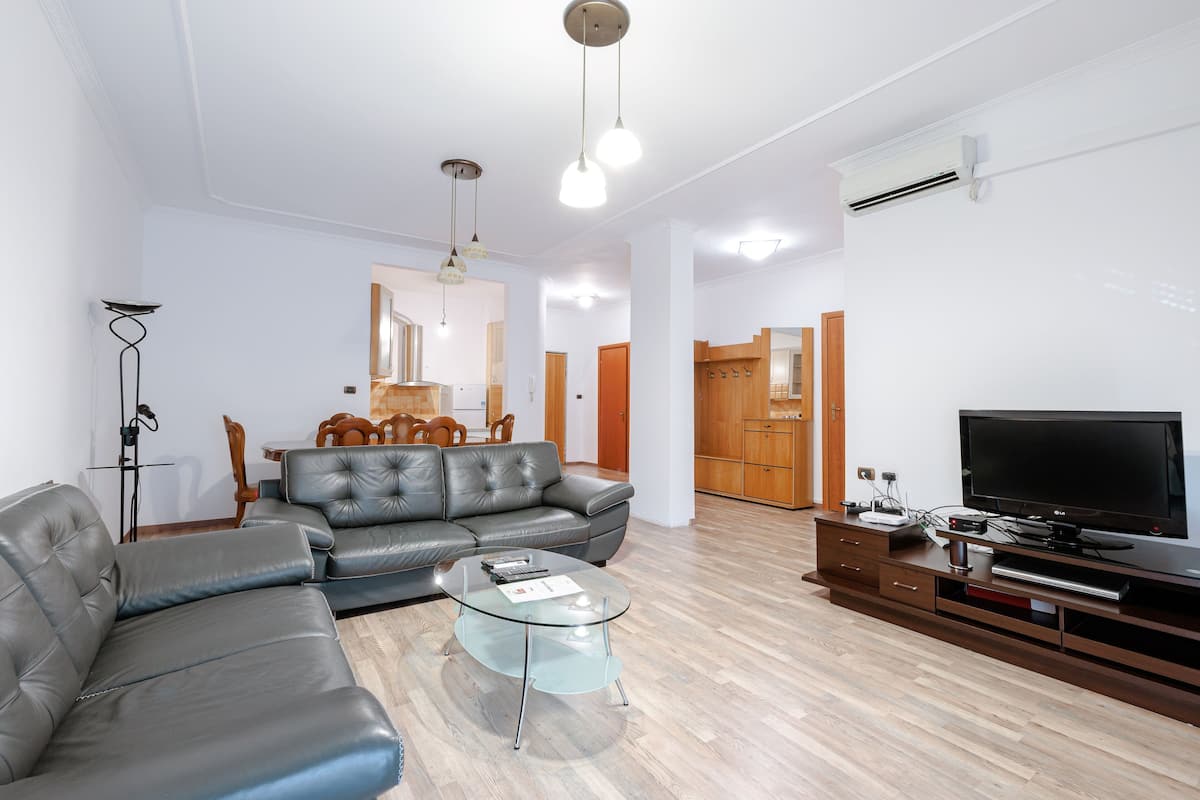 Ein modernes Wohnzimmer mit Ledersofa, Glastisch, Holzunterhaltungseinheit und Flachbildfernseher.
