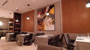 A modern dining area with tables set for service, a large abstract painting on the wall, and a television in the background. - Boutique Hotel Whisky (Tirana)