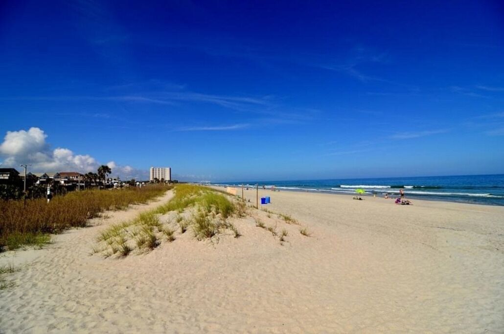 A beach with a clear sky, sandy shore, and buildings in the background.