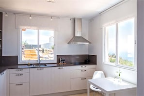 Une cuisine moderne dotée d’une grande fenêtre, d’une hotte en acier inoxydable et offrant une vue sur l’extérieur.