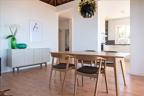 Un espace repas moderne avec une table et des chaises en bois, un meuble blanc et un vase vert orné de fleurs.