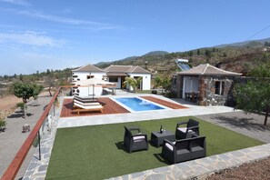 A pool area with artificial grass, outdoor furniture, and a stone building with a tiled roof. - Casa La Florida en Puntagorda (Tijarafe)