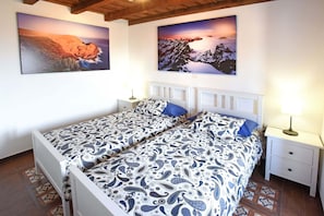 A double bed with a patterned bedspread, a bedside table with a lamp, and two wall-mounted paintings of landscapes.
