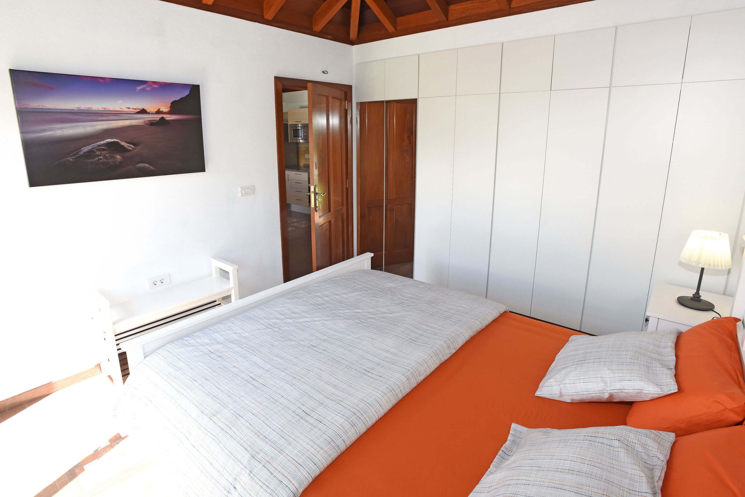 A bedroom with a bed, a nightstand, a lamp, a wardrobe, and a painting on the wall.