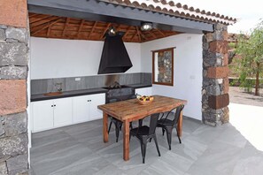 Eine Außenküche mit Holztisch und -stühlen, Steinwänden und einem gefliesten Boden.