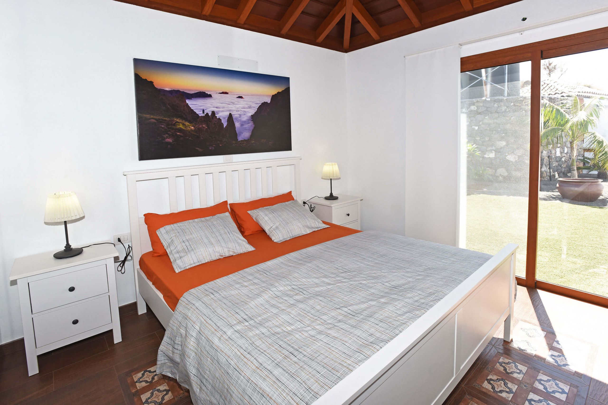 Une chambre à coucher comprenant un lit, deux tables de chevet, une commode, une fenêtre donnant sur l’extérieur et un tableau accroché au mur.