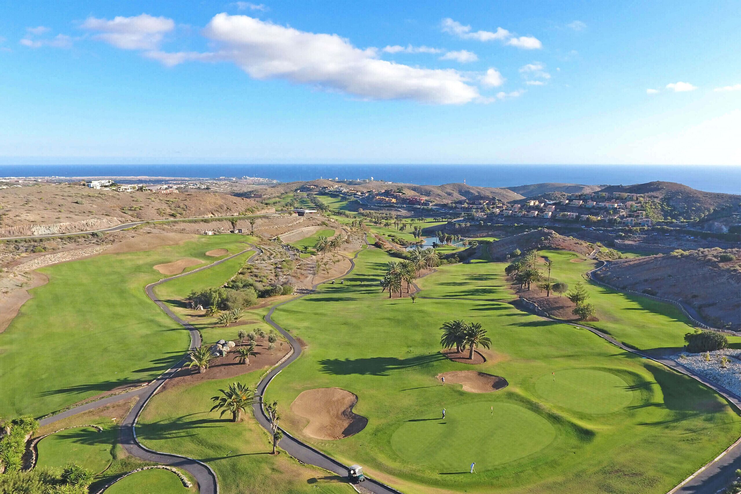 A golf course with a clear view of the ocean and distant hills.