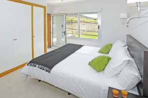 A bedroom with a bed, a view through a sliding door, and a nightstand with glasses. - Salobre Vista Golf 30 (Maspalomas)