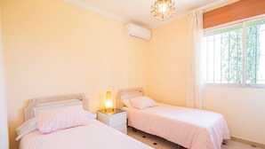 Una camera da letto con due letti, un comodino con una lampada, un condizionatore d'aria e una finestra con tende.