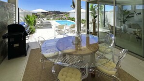 Un patio cubierto con vidrio, una piscina, sillas transparentes y una parrilla.