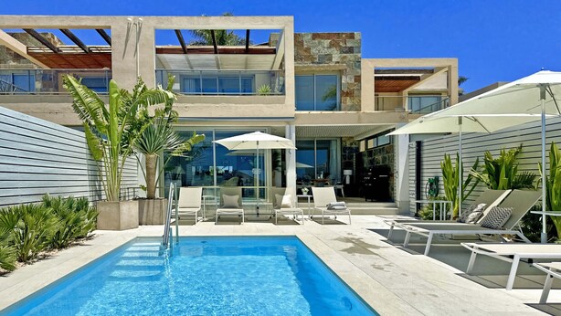 Un área de piscina moderna con una piscina rectangular, sillas de descanso y sombrillas.