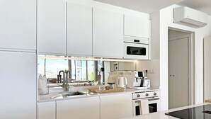 Una cocina moderna con armarios blancos, microondas integrado, cafetera y estufa.