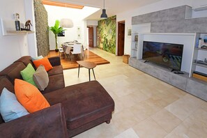 Ein modernes Wohnzimmer mit einer braunen Ledersofa, einem Flachbildfernseher und einem Essbereich im Hintergrund.