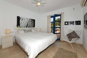 Una camera da letto con un letto grande, una ventola a soffitto, una finestra con tende, una sedia e una mensola a parete con un'opera d'arte a motivi zebrati.