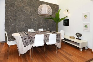 Ein Essbereich mit Steinwand, einem Tisch mit weißen Stühlen, einer großen Pflanze und Wandleuchten.
