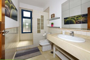 Un bagno con un lavandino bianco, un water, una finestra e decorazioni murali con cactus.