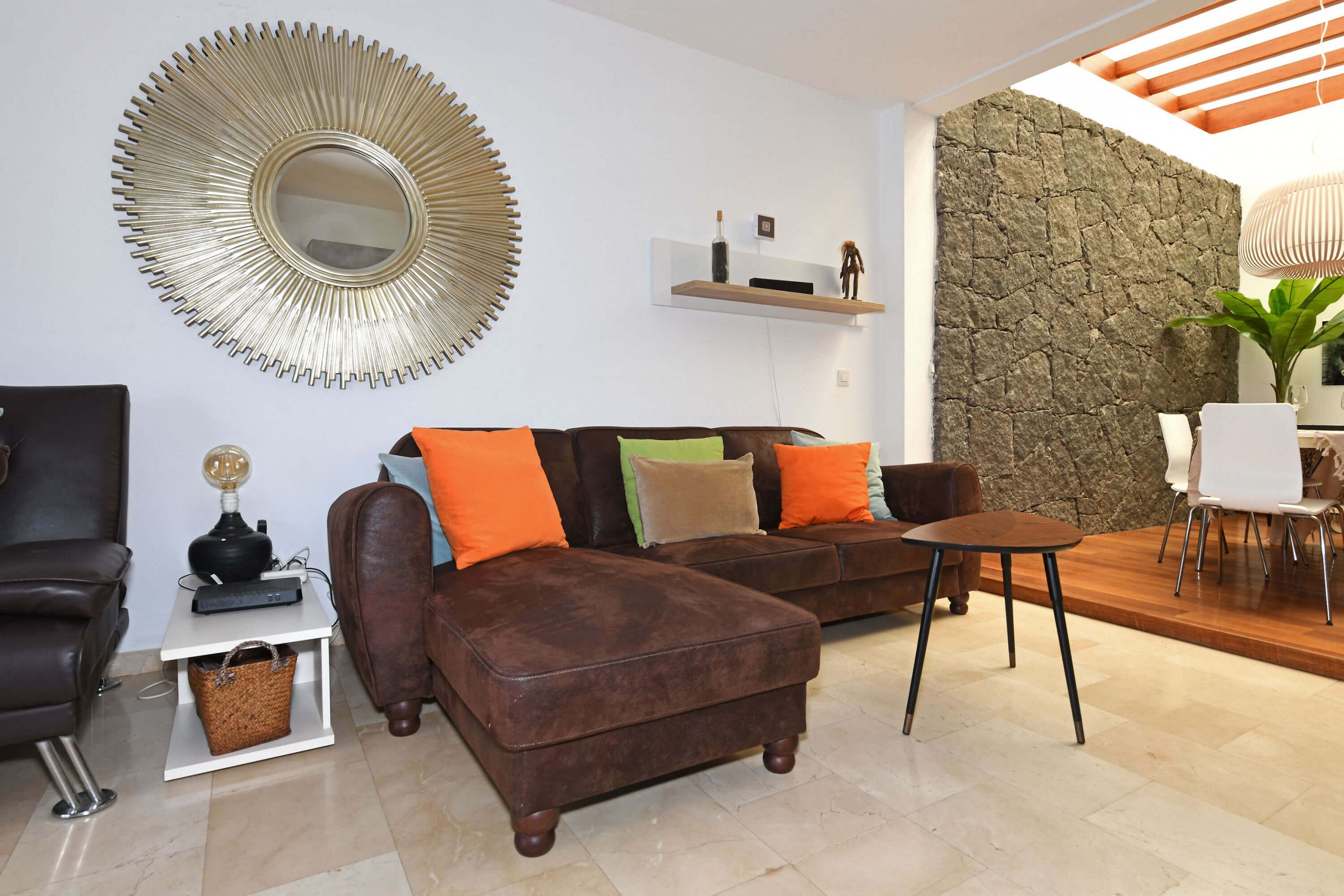 Ein modernes Wohnzimmer mit einem braunen Ledersofa, einem runden Spiegel und einer Wand mit Steinverkleidung.