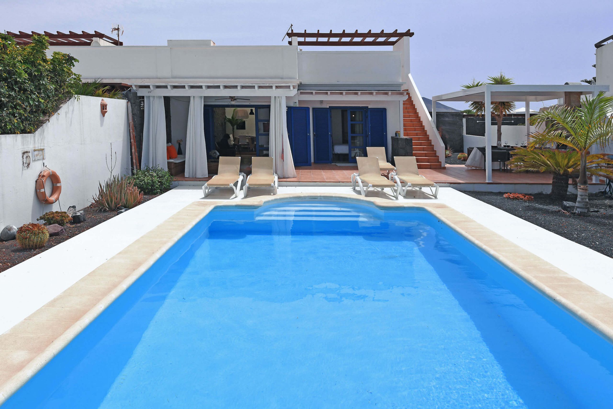 A modern pool area with a clear blue pool, lounge chairs, and a covered patio.