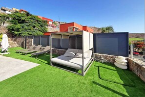 A modern outdoor bedroom with a canopy bed, lounge chairs, and a stone wall. - Salobre Vista Golf 16 (Maspalomas)