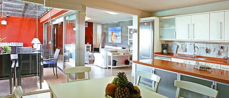 A modern kitchen with white cabinets, a dining area with a table and chairs, and a fruit bowl on the table.