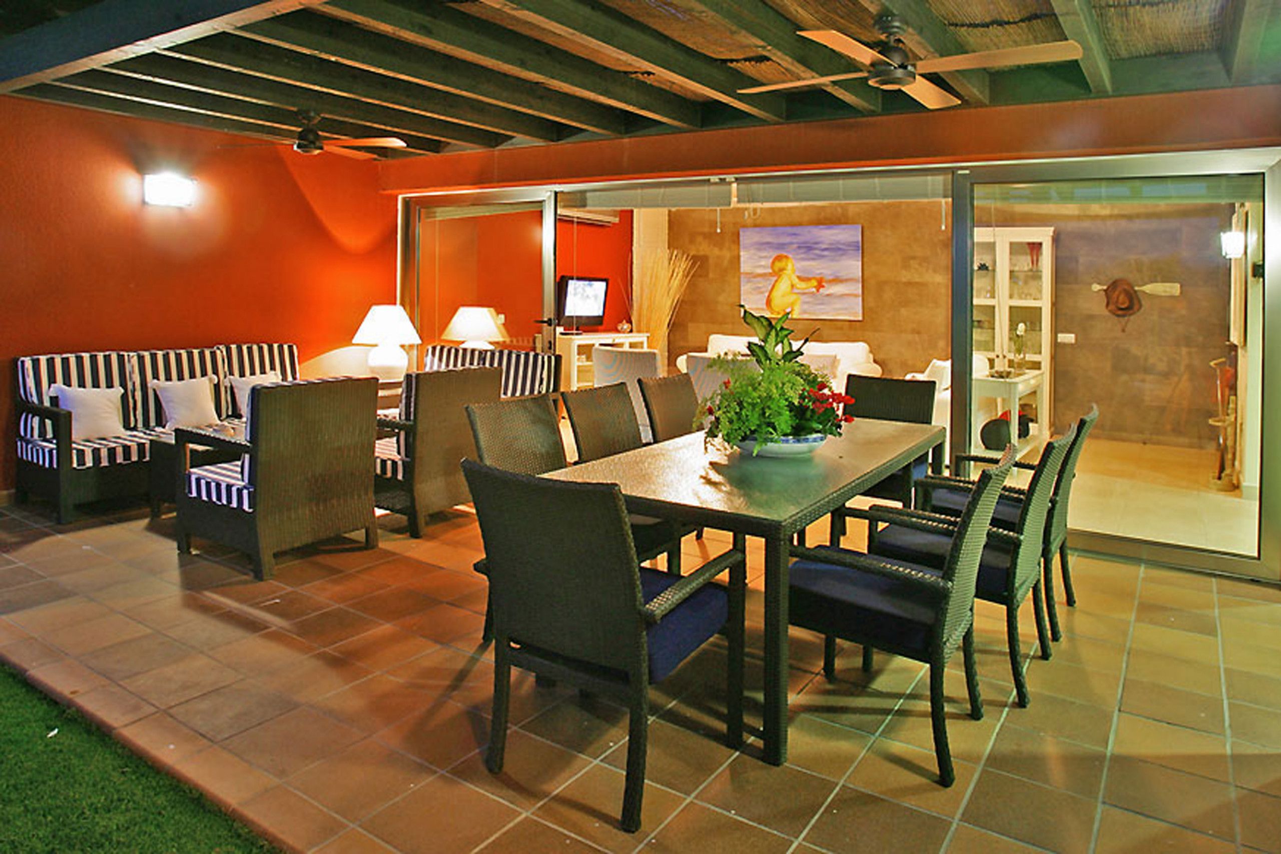 An outdoor dining area with a table and chairs, a TV, and a painting on the wall.