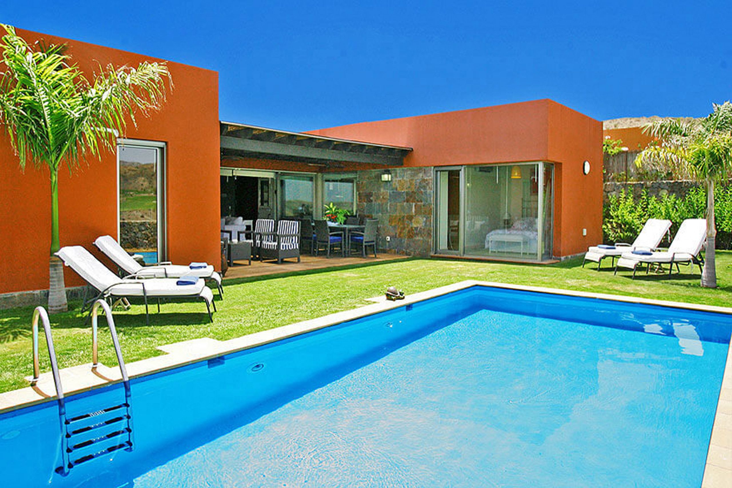 Ein moderner Poolbereich mit klarem, blauem Pool, Liegestühlen und einer Terrasse mit Gartenmöbeln.