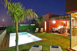 A swimming pool with two lounge chairs, a patio area with outdoor furniture, and a glass-enclosed dining area. - Villa Salobre Par 4 N° 22 (Maspalomas)