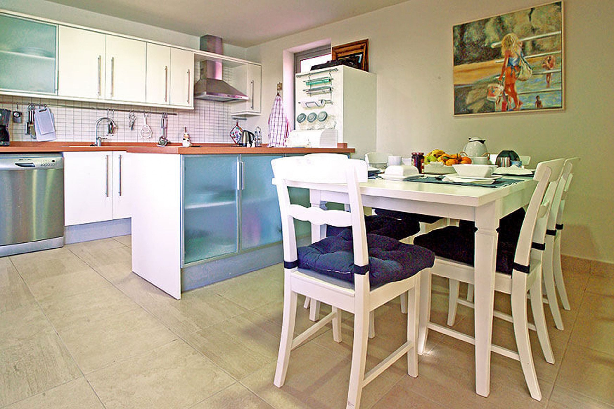 Una cocina con armarios blancos, lavavajillas y un comedor con mesa y sillas blancas.