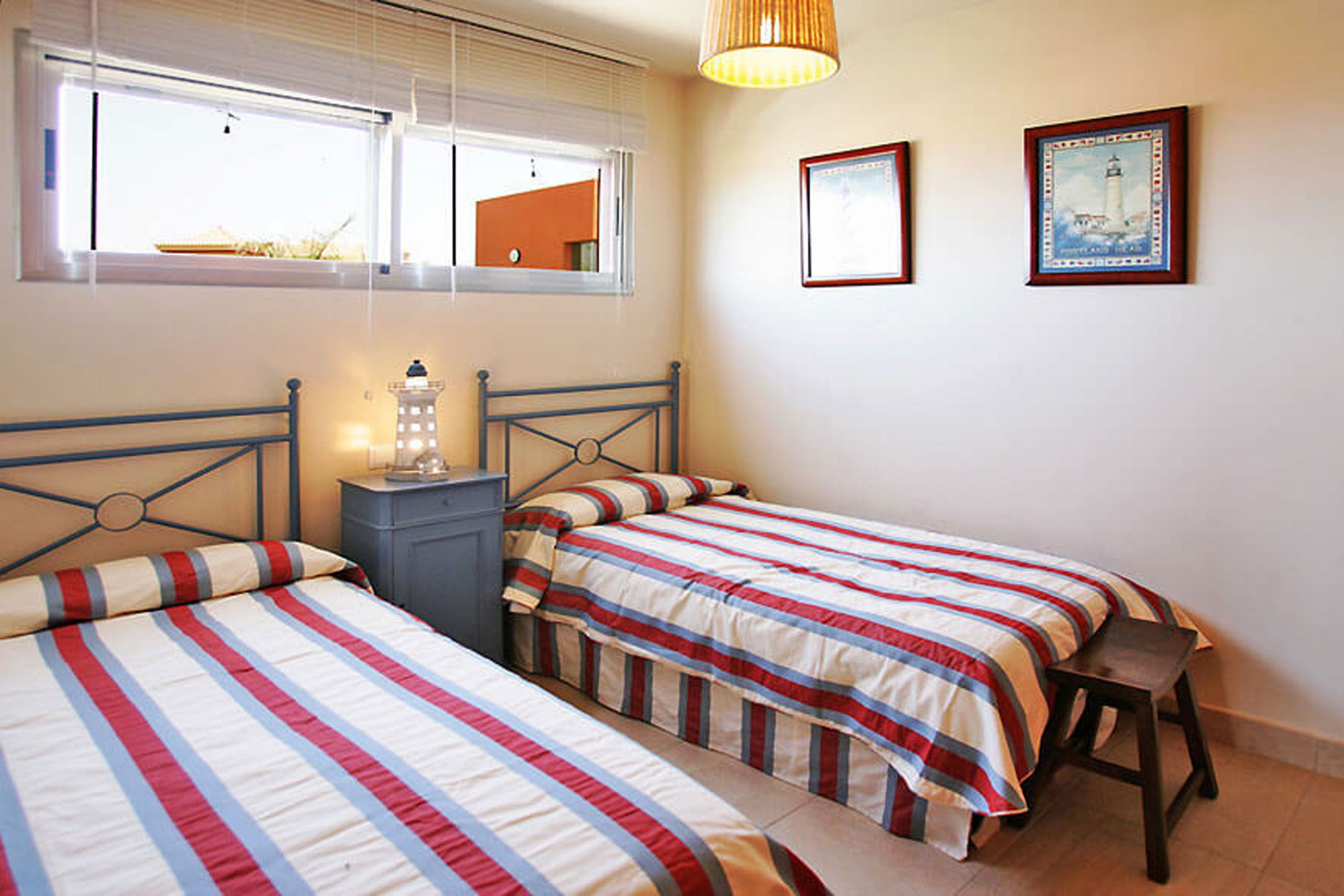 Un dormitorio con dos camas, una mesita de noche, una lámpara y una ventana con persianas.