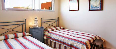 Un dormitorio con dos camas, una mesita de noche, una lámpara y una ventana con persianas.