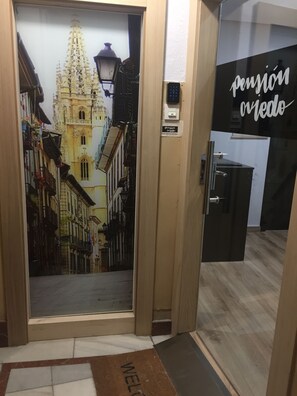 A hotel entrance with a decorative door featuring a historical building mural, a digital lock, and a welcome mat. - Pension Oviedo (Oviedo)